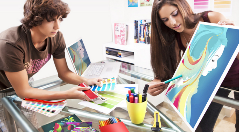 Two people working together on a colorful artwork project at a desk.