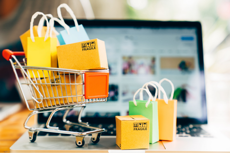 A miniature shopping cart filled with colorful bags and boxes sits on top of a laptop keyboard.